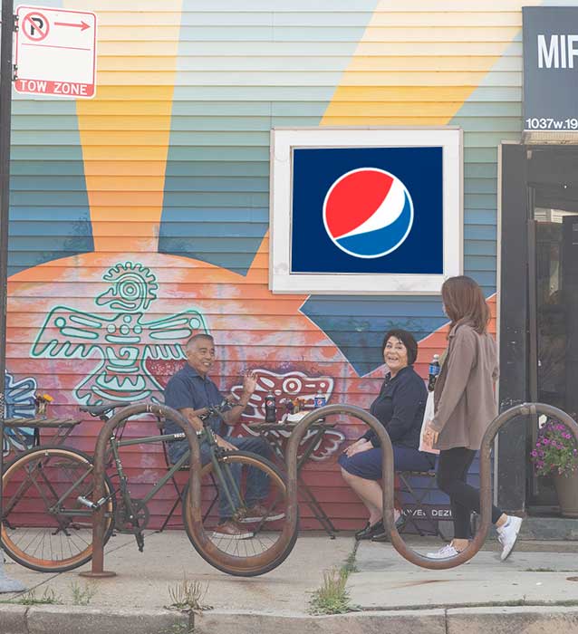Two people sitting in front of a corner store talking to a woman passing by.
