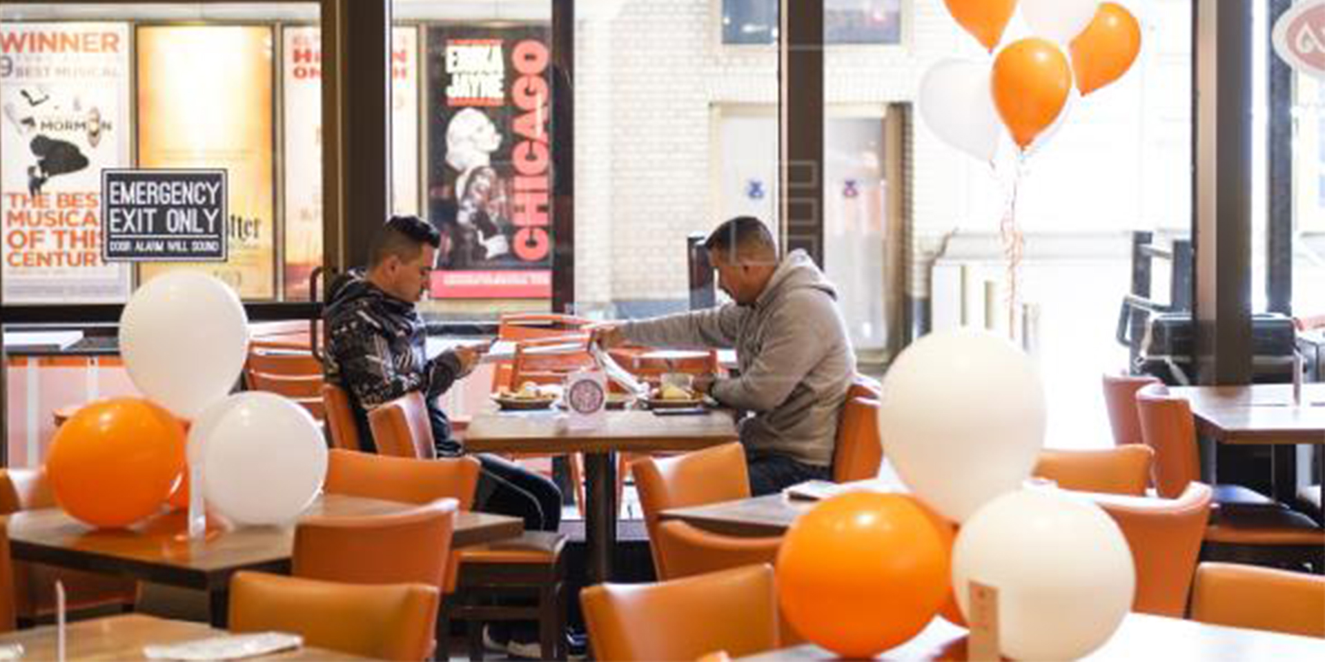 Men sitting in an empty restaurant with white and orange balloons.