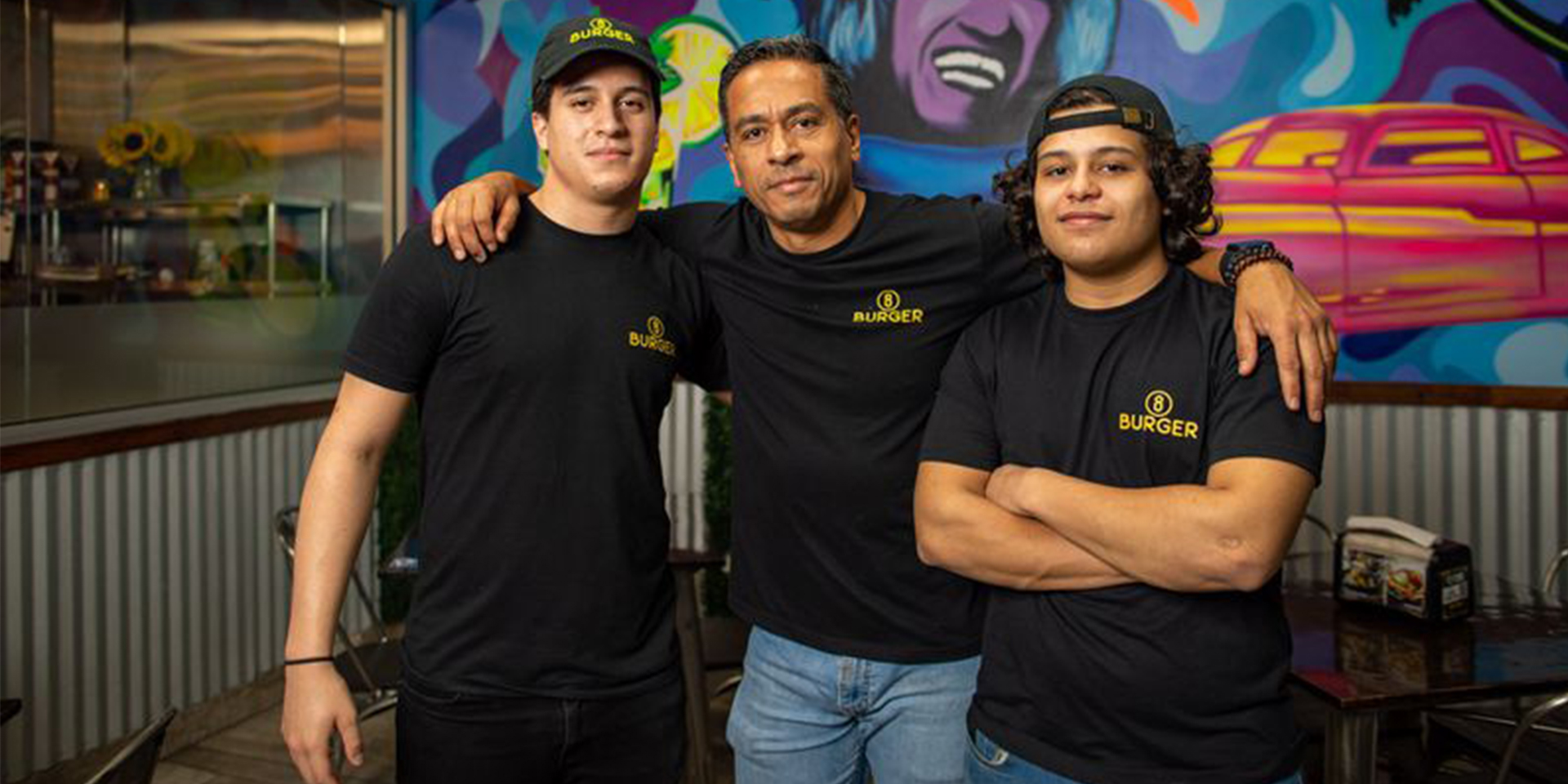 Staff at a restaurant wearing matching black shirts with a colorful background.