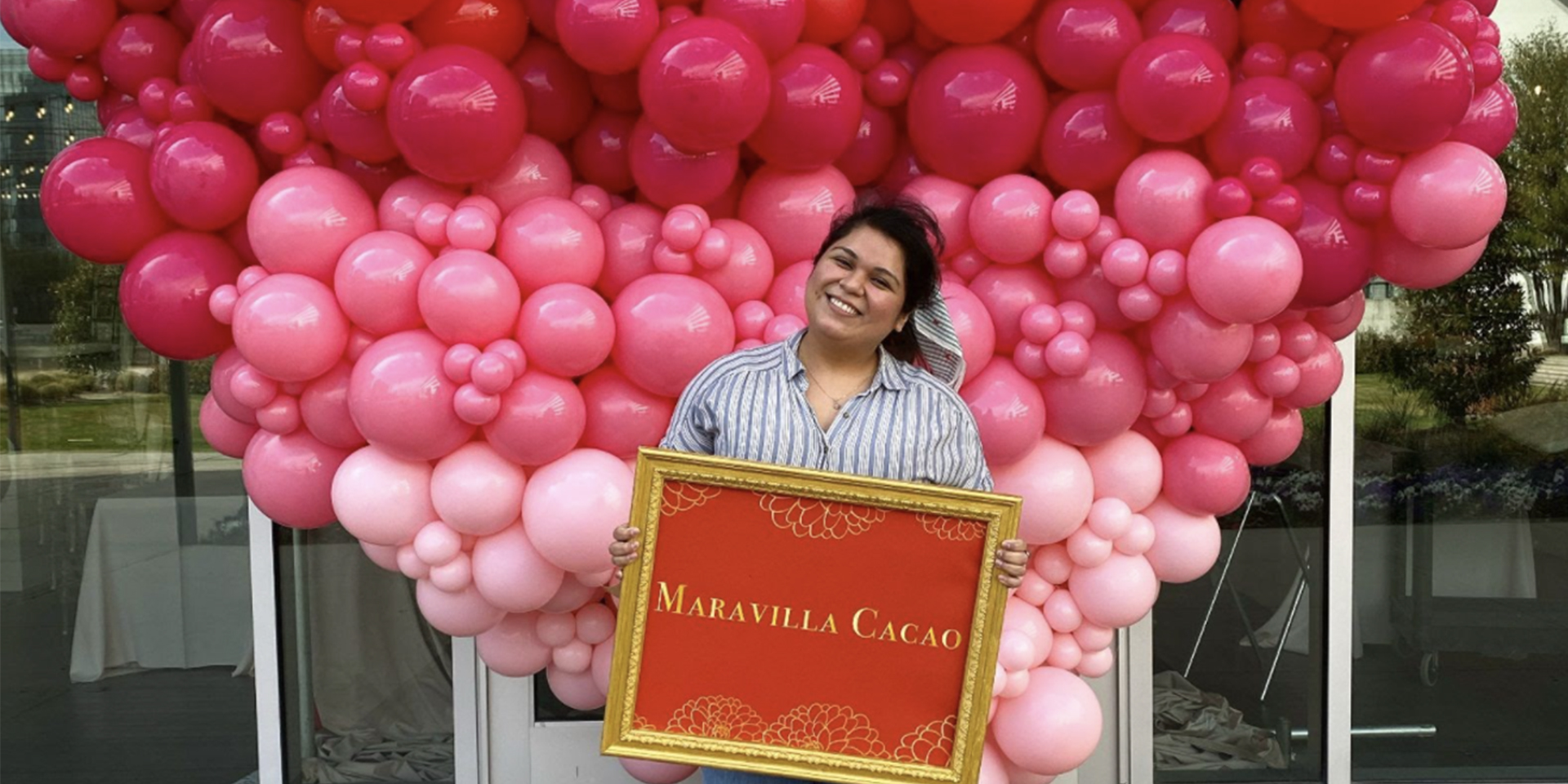 Smiling woman holding a sign with pink and red balloons in the background.