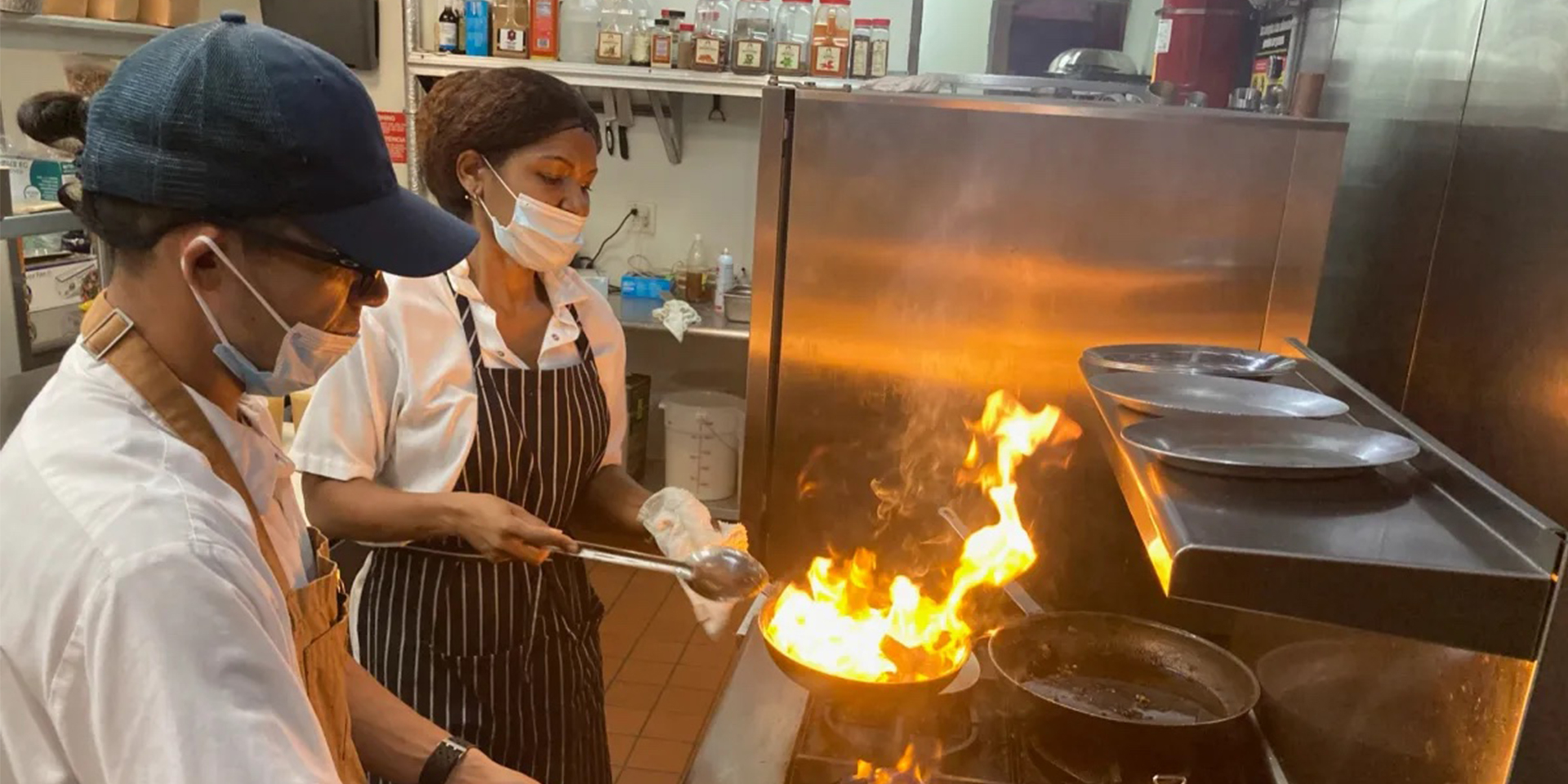 Cooks doing flambe on food in a restaurant kitchen.